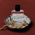 Perfume bottle by Kismet Olfactive labeled 'Nymphéas' on a decorative tray with gold accents against a red background