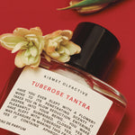 Perfume bottle labeled 'Tuberose Tantra' by Kismet Olfactive with flowers on a red background